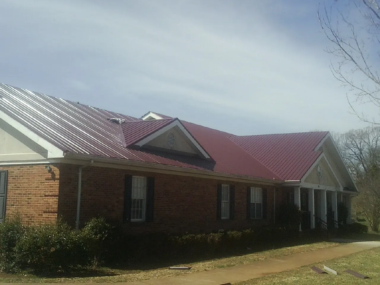 Red metal roof with gabled entries on a long brick building, from a Hail Damage Roof Repair job in Canyon