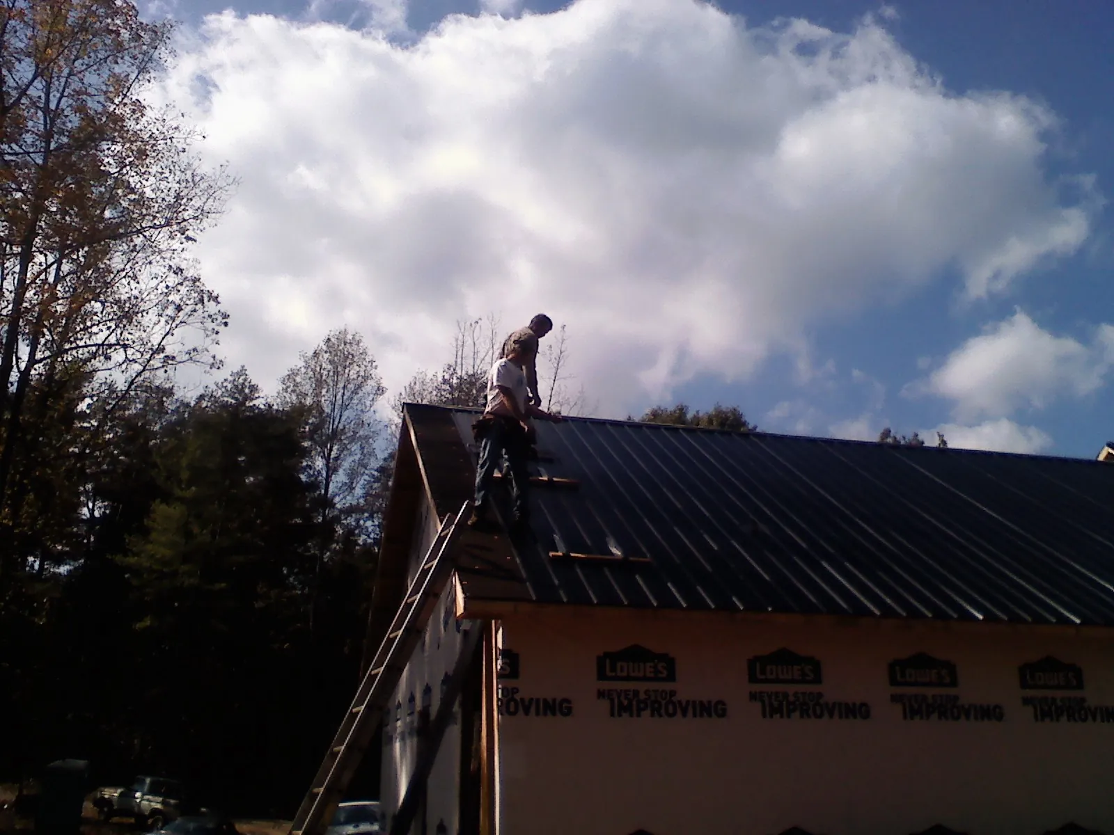 Roofer fastening dark metal panels high against a cloudy sky, from a Roof Inspection job in Canyon